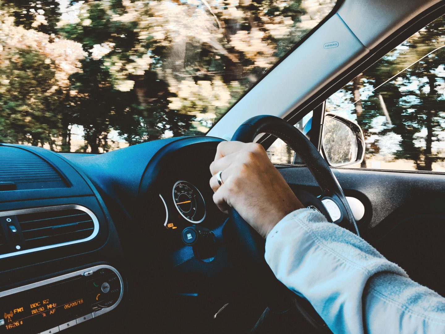 Die Hand des Fahrers am Lenkrad eines modernen Autos während einer Tagesfahrt durch eine malerische Landschaft.