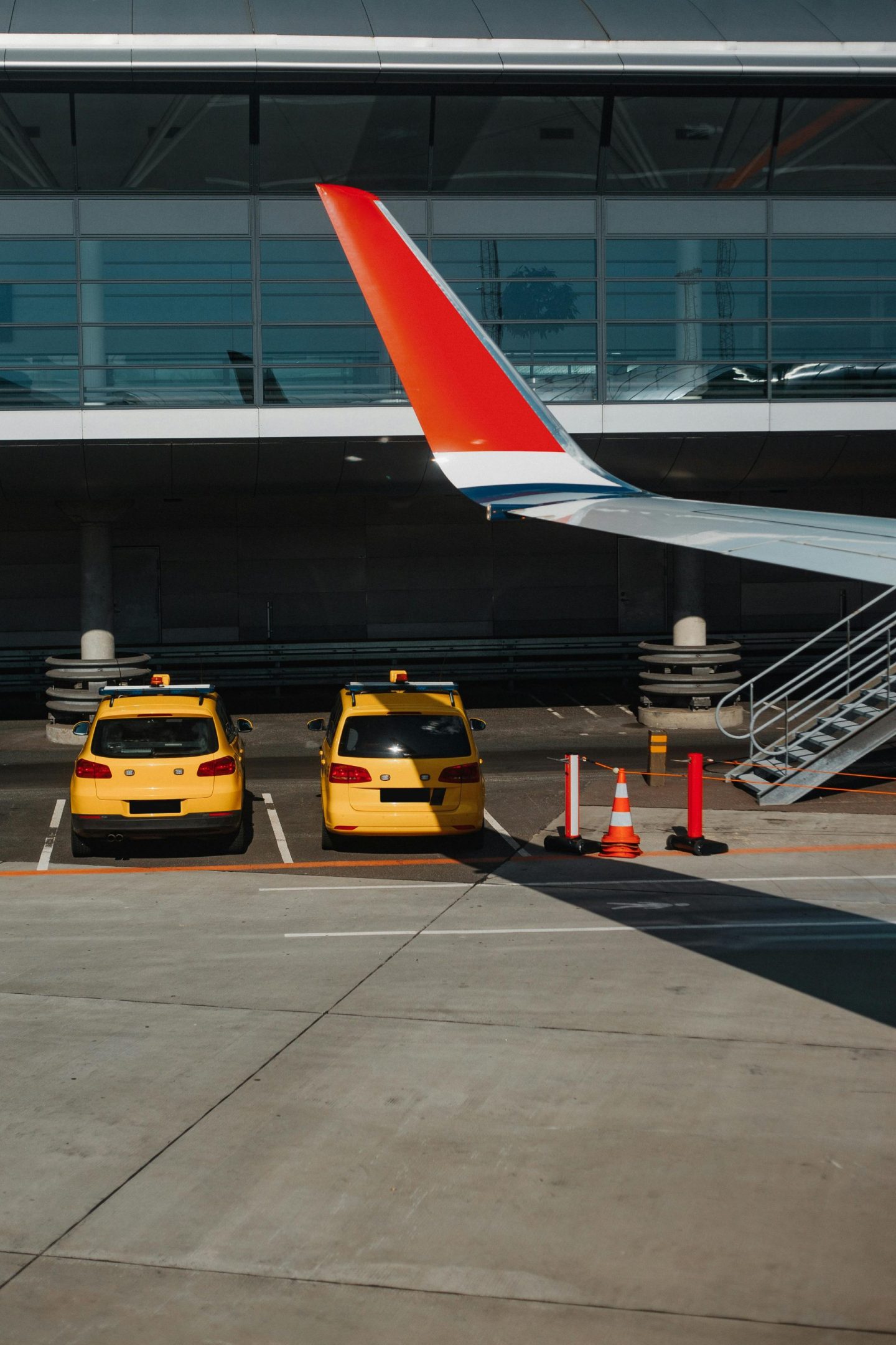 Zwei gelbe Taxis parken unter einem Flugzeugflügel auf einem städtischen Flughafen.