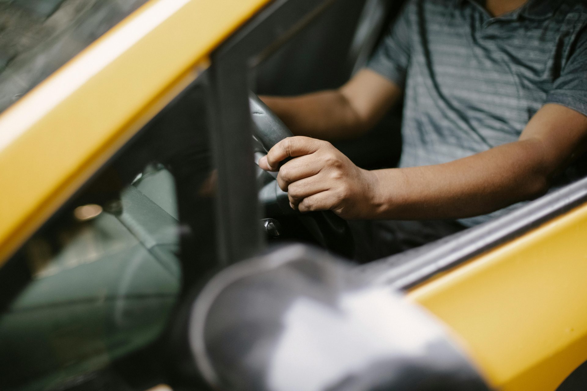 Von oben ist ein nicht erkennbarer Mann in einem Poloshirt zu sehen, der tagsüber in einer Stadtstraße ein gelbes Taxi fährt.
