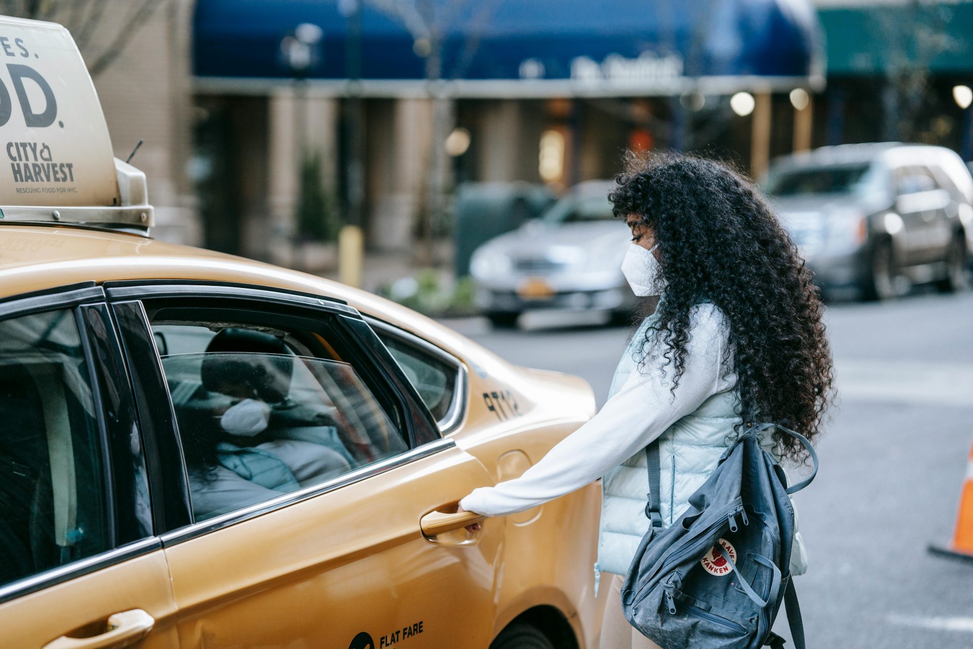 Seitenansicht einer nicht erkennbaren afroamerikanischen Frau mit langen dunklen Haaren in Freizeitkleidung und mit medizinischer Maske, die die Tür eines auf der Straße geparkten Autos öffnet.